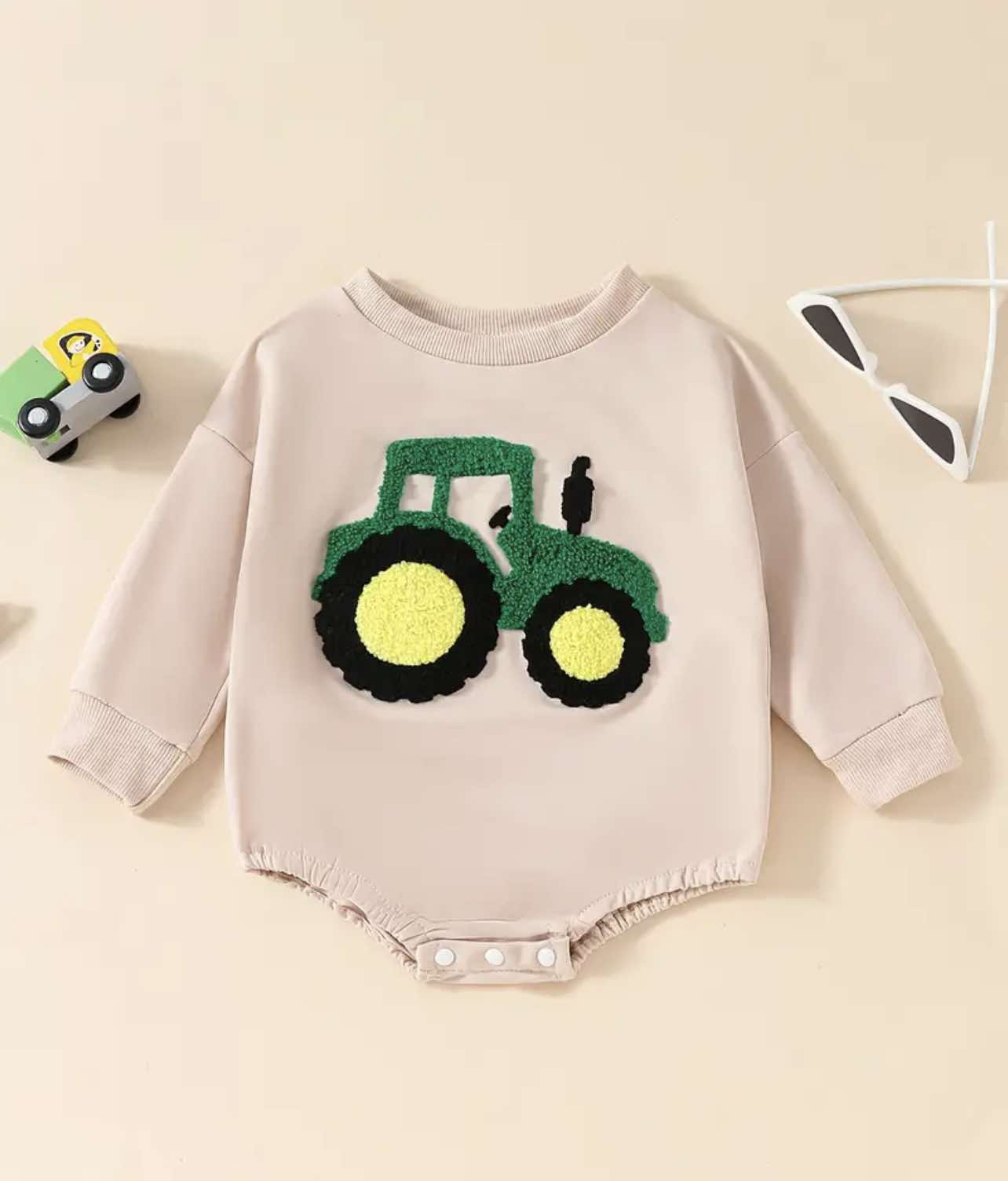 Baby wearing the Tractor Embroidered Onesie, sitting on a cozy blanket with a toy tractor.