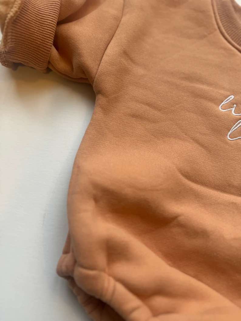 Close-up of 'Little Love' embroidered on fleece-lined cotton romper in burnt orange