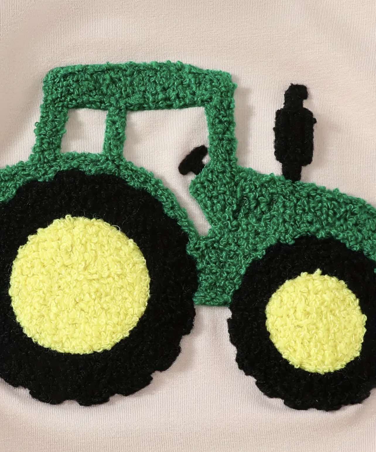 Close-up of the embroidered tractor detail on the front of the beige baby onesie.