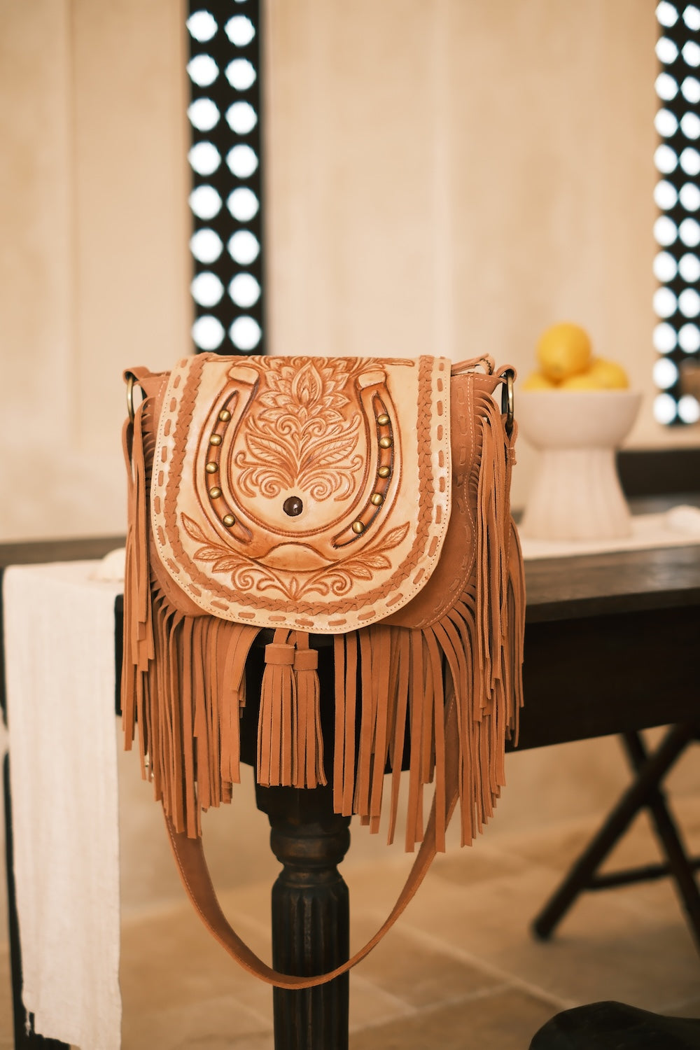Genuine leather Kimberley Horseshoe Bag in tan with brass hardware, tassel, and hand‑carved horseshoe motif.