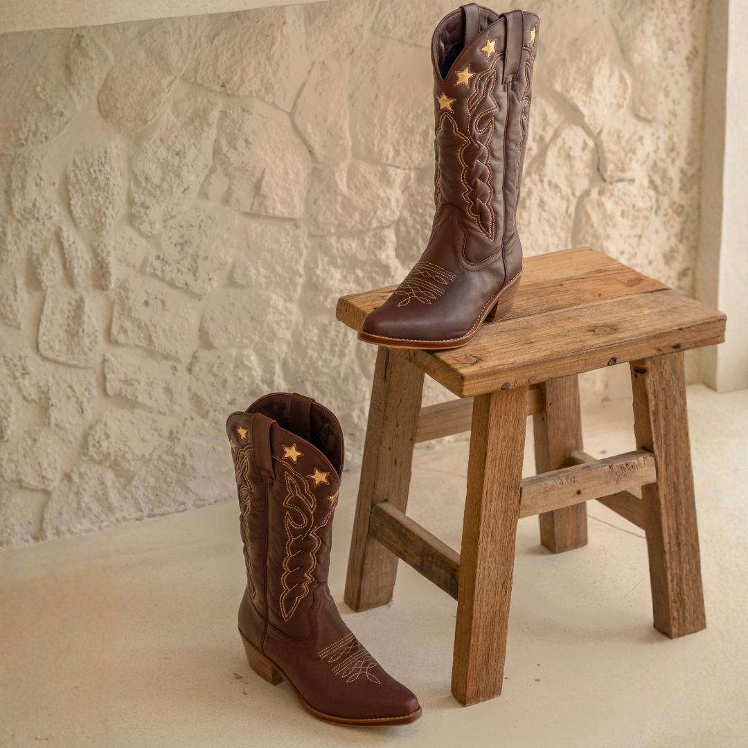 Lone Star Boots from House of Hide in dark brown leather with tan western embroidery and star details being displayed on rustic wooden stool and floor against light stone wall