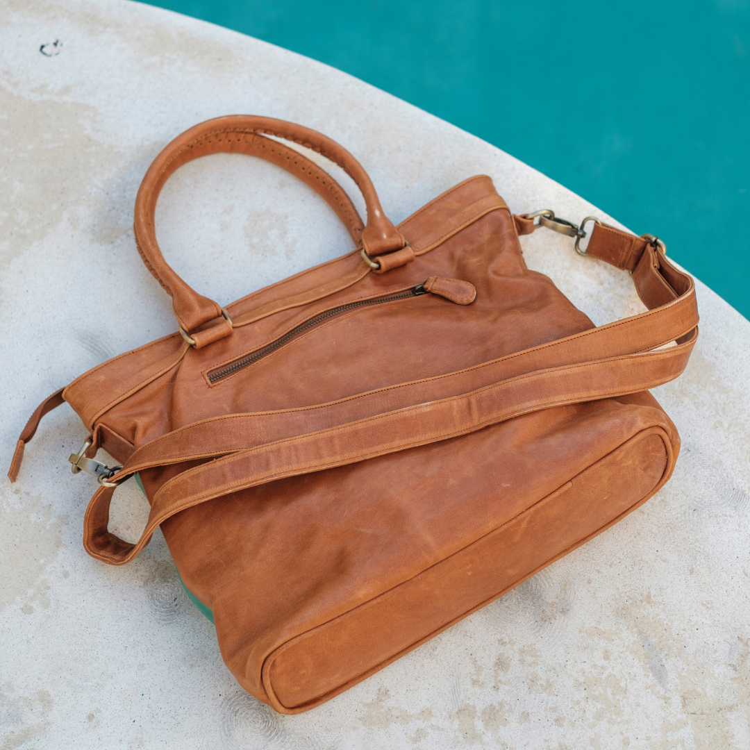 Mesa Sunset Tote Bag from House of Hide in tan leather with dual top handles and detachable shoulder strap being displayed on light stone surface with turquoise pool in background