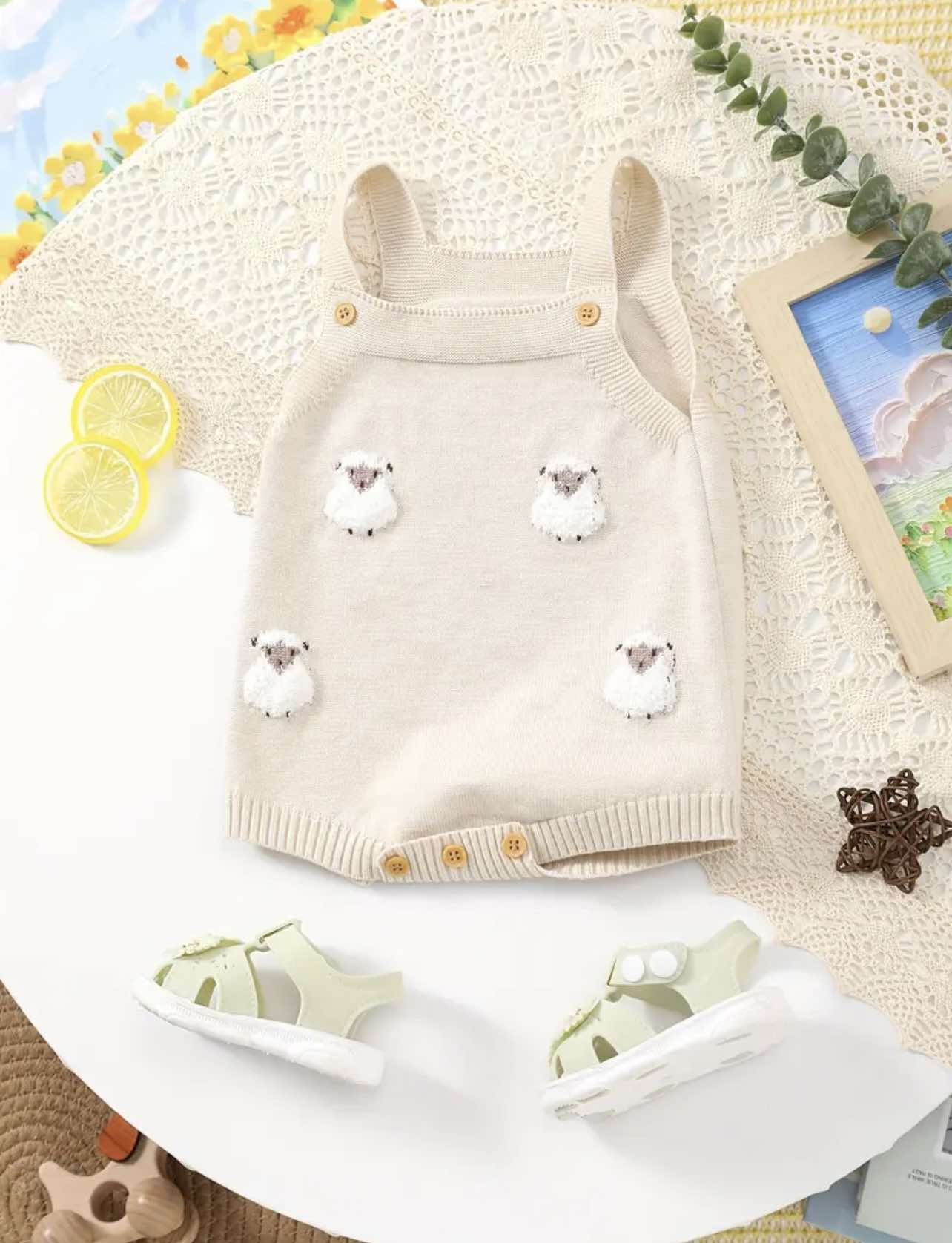 Neutral knit baby romper with embroidered lambs and wooden buttons, laid flat with toddler sandals