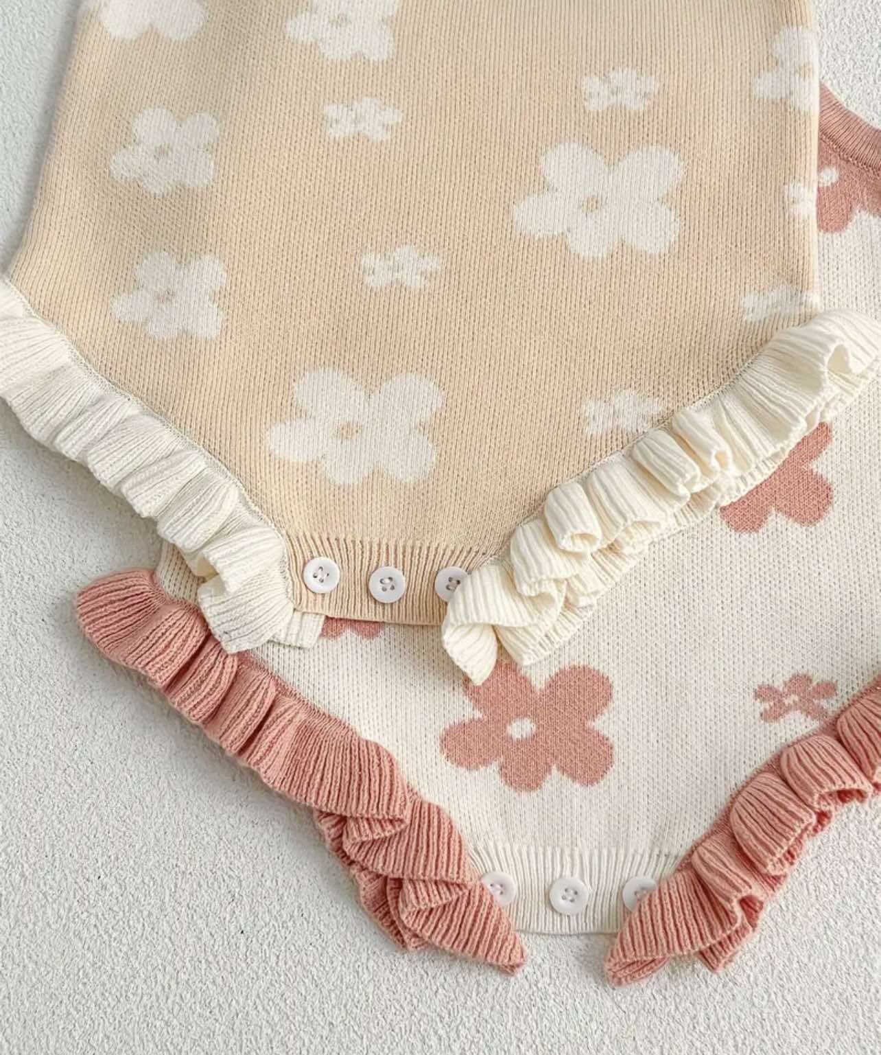 Pink floral knitted romper for baby girls, sleeveless with delicate straps, laid flat on a white background.