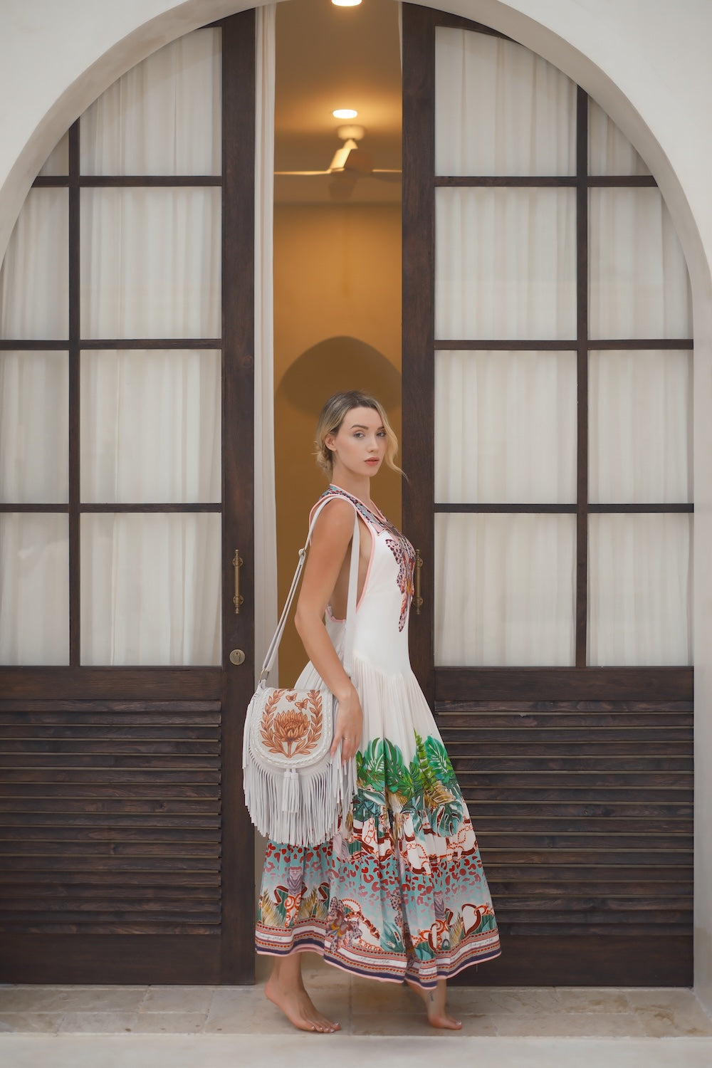 Protea Bloom Bag in off‑white leather with hand‑tooled floral design, fringe, and brass hardware. Crossbody with zip and magnetic closure. Ethically handmade.