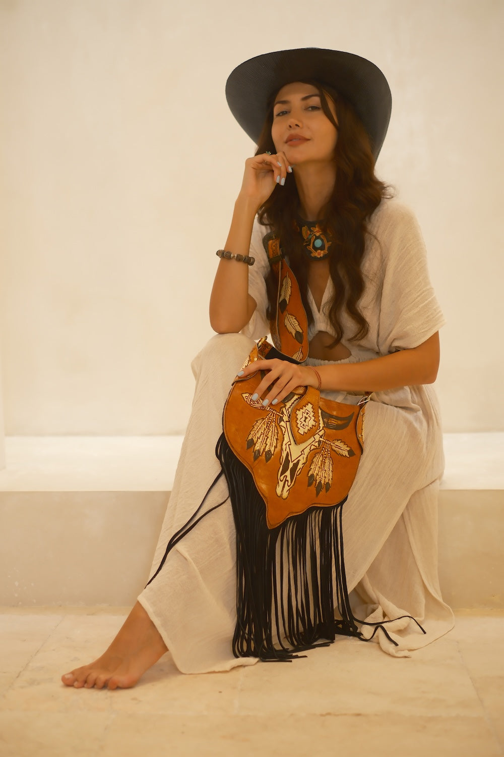 Western-inspired black leather fringe bag featuring floral tooled details, adjustable strap, and roomy compartments.