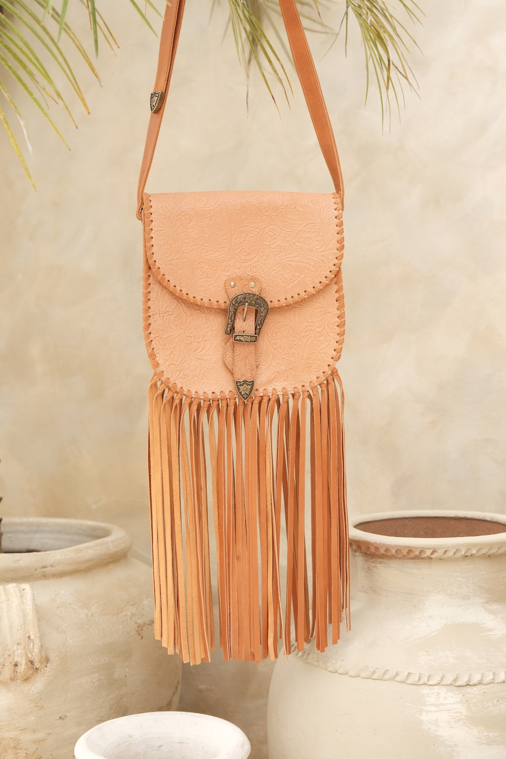 Peach-colored fringe bag with a decorative clasp on a neutral background