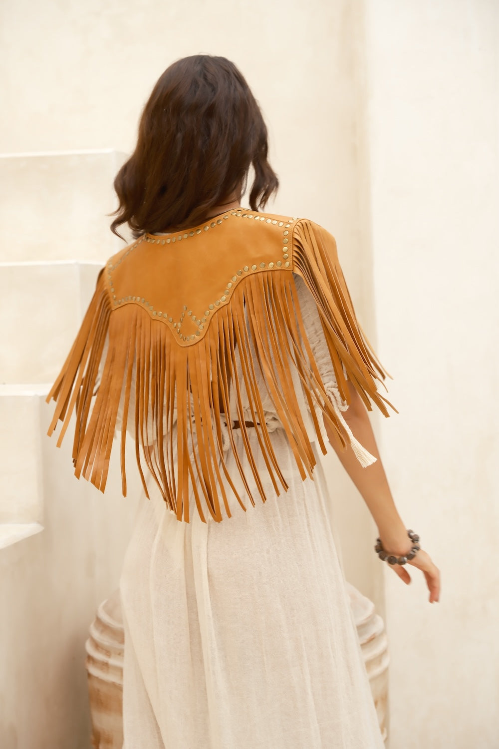 Back view of cropped Western bolero with leather tassels. Handcrafted leather bolero with gold studs and hand-cut fringe, worn with denim for modern Australian rodeo fashion.