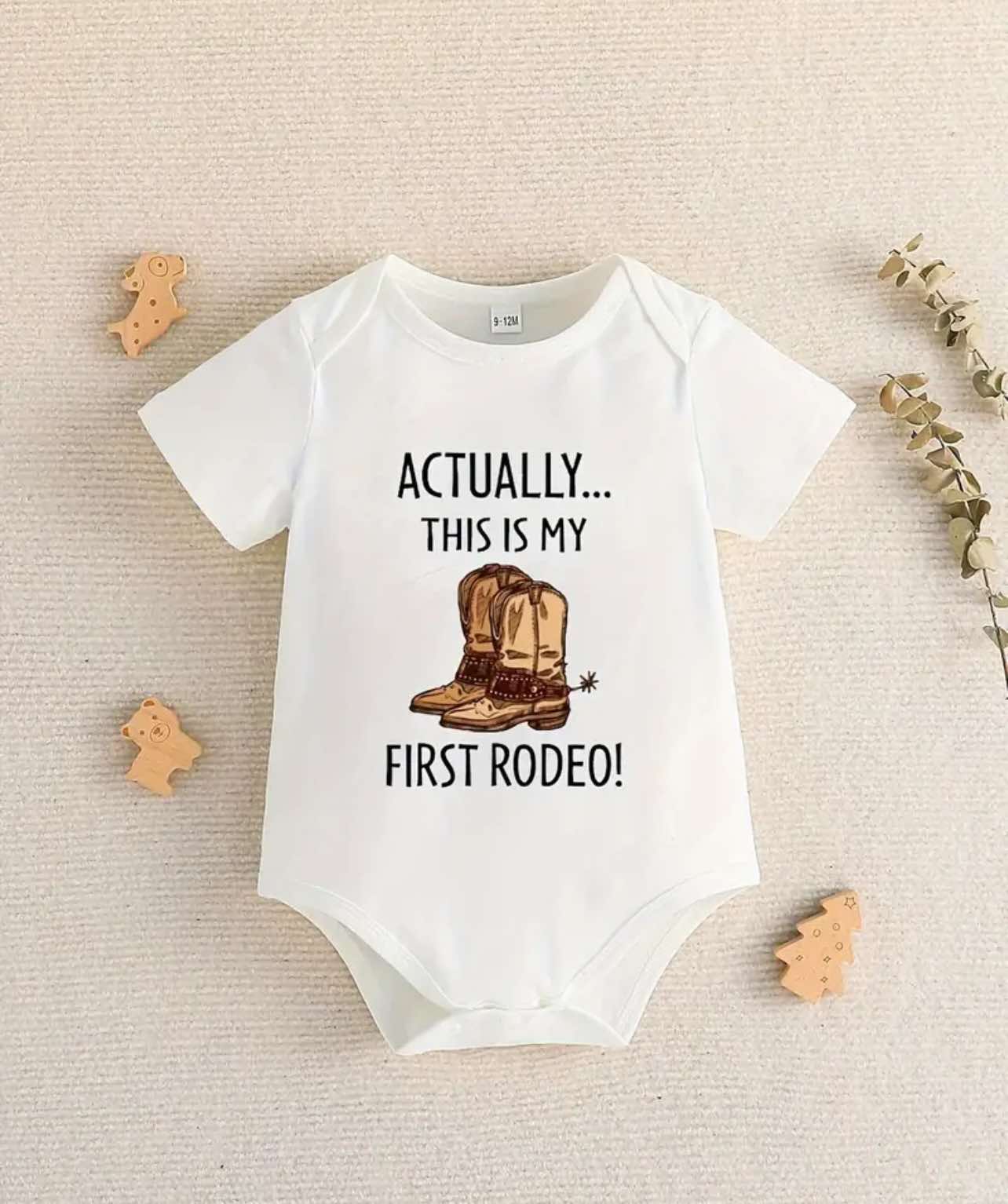 Smiling baby dressed in a Western cowboy onesie with "Actually This Is My First Rodeo" print.
