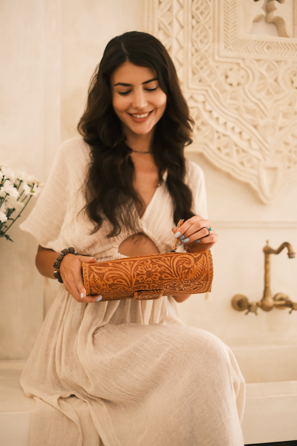 Handcrafted from rich tobacco leather, this versatile clutch features floral tooling, bronze hardware, a detachable strap, and artisan detailing. Perfect for markets, dinners, and events.