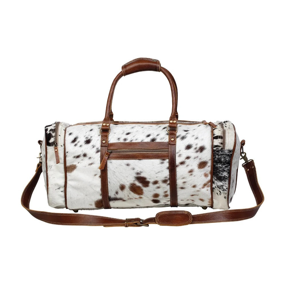 House of Hide genuine leather western duffel bag with a brown and white cow print pattern, premium brown leather straps, and travel-ready design on a white background
