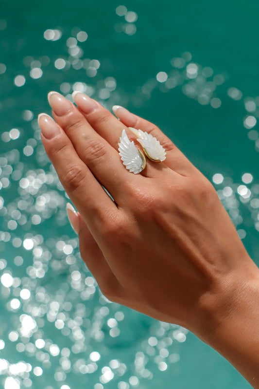 Hand with shell-themed jewelry against a sparkling water background