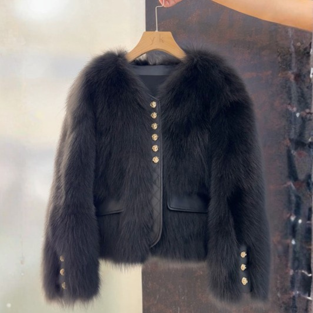 Bailey Jacket from House of Hide in plush black faux fur with gold-tone decorative button closures, vegan leather placket trim, full voluminous sleeves, cropped boxy silhouette being displayed hanging on wooden hanger against split light and dark background