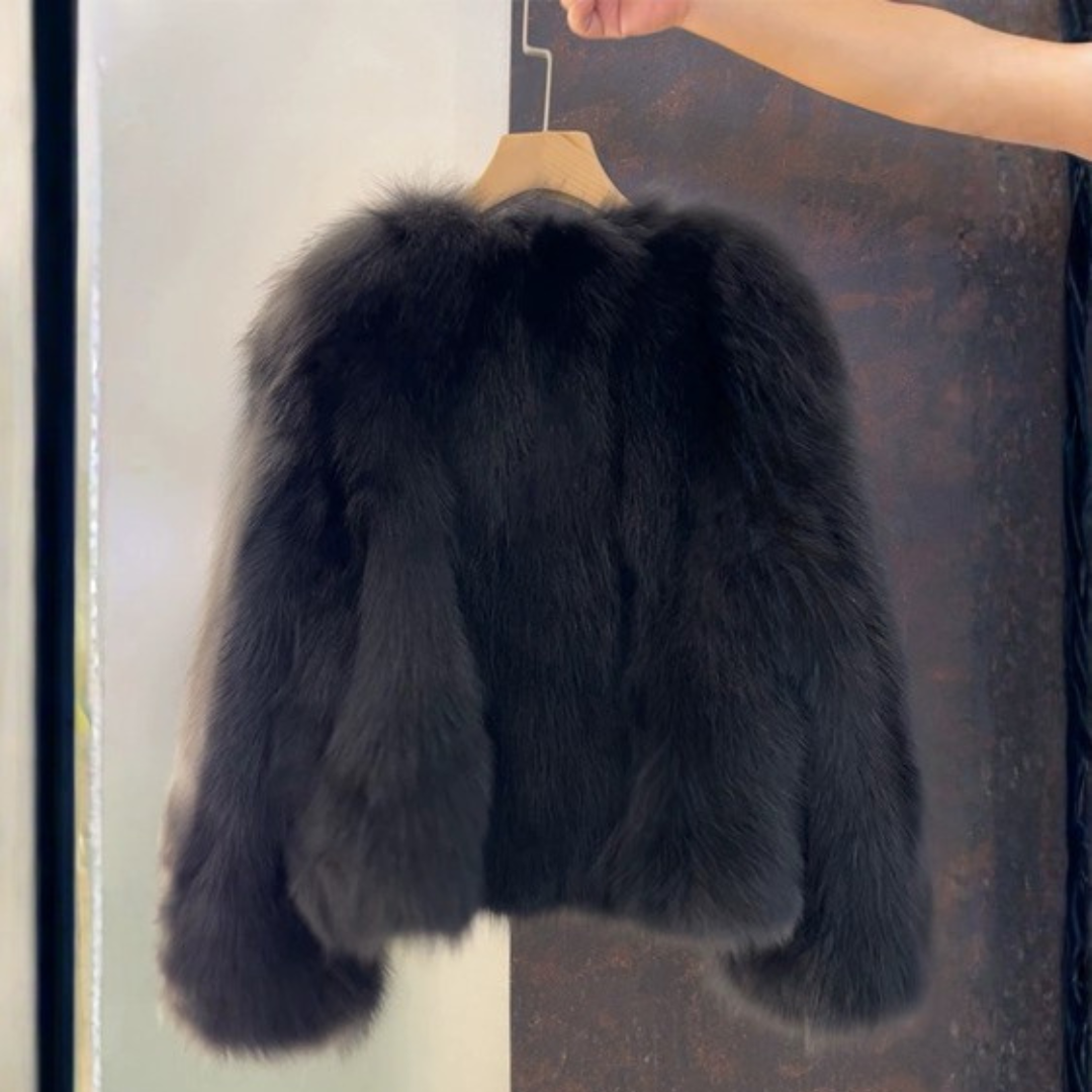 Bailey Jacket from House of Hide in plush black faux fur with gold-tone button closures, vegan leather placket and pocket trim, full voluminous sleeves, cropped boxy silhouette being held on wooden hanger by model's hand in editorial lifestyle shot