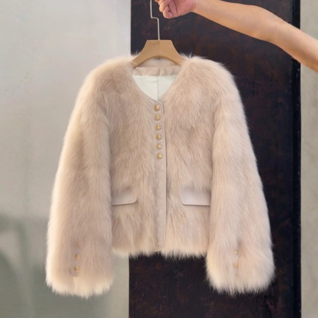 Bailey Jacket from House of Hide in plush cream faux fur with gold button closures, vegan leather placket and pocket trim, full voluminous sleeves, cropped boxy silhouette being held on wooden hanger by model's arm against split gray and black background
