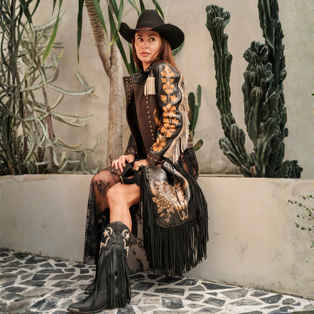 Bindi Fringe Bag from House of Hide in black leather with fringe detail being held by model wearing black cowboy hat and black fringed cowboy boots in garden setting with cacti