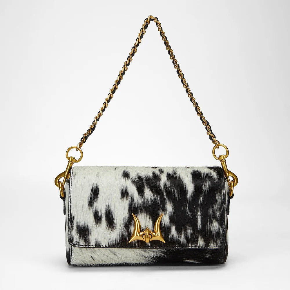 House of Hide genuine leather black and white cow print handbag featuring a gold chain handle on a light gray studio background