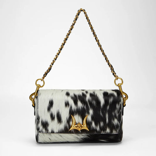House of Hide genuine leather black and white cow print handbag featuring a gold chain handle on a light gray studio background