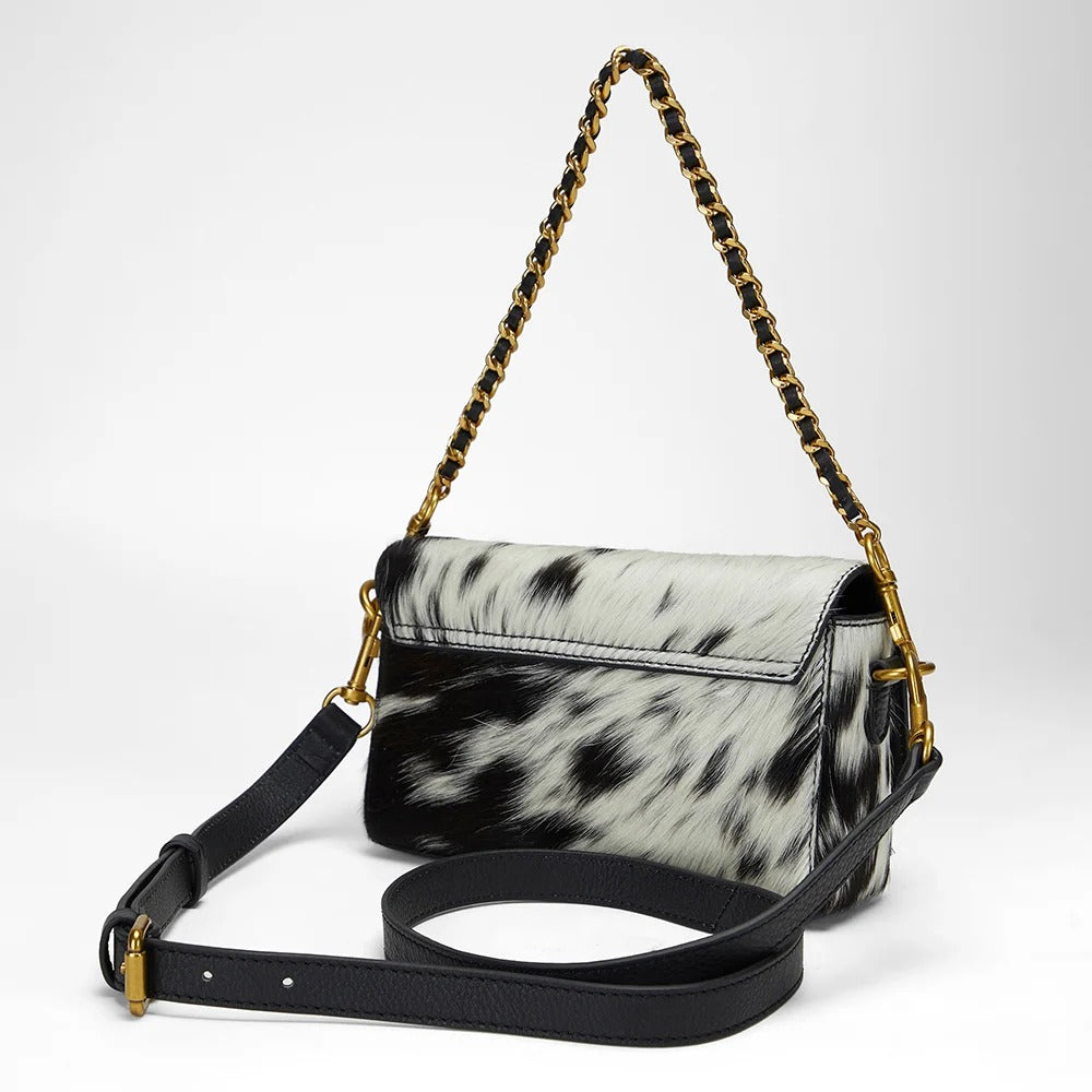 House of Hide genuine leather black and white cowhide handbag featuring a gold-tone chain strap on a light gray studio background