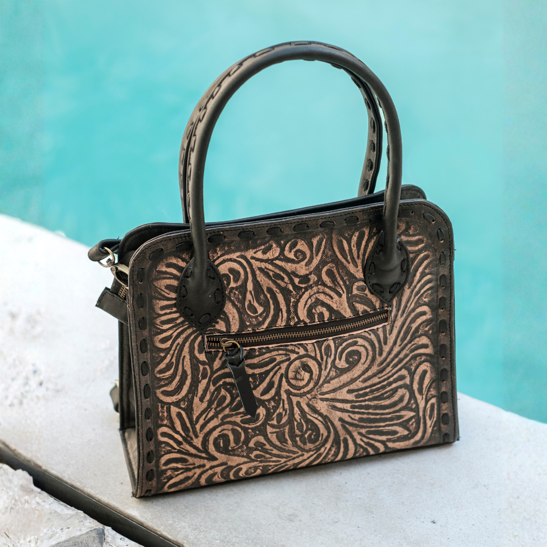 Blackwood Shoulder Bag from House of Hide in light tan leather with dark brown tooled leather detailing being displayed on stone ledge with turquoise water background