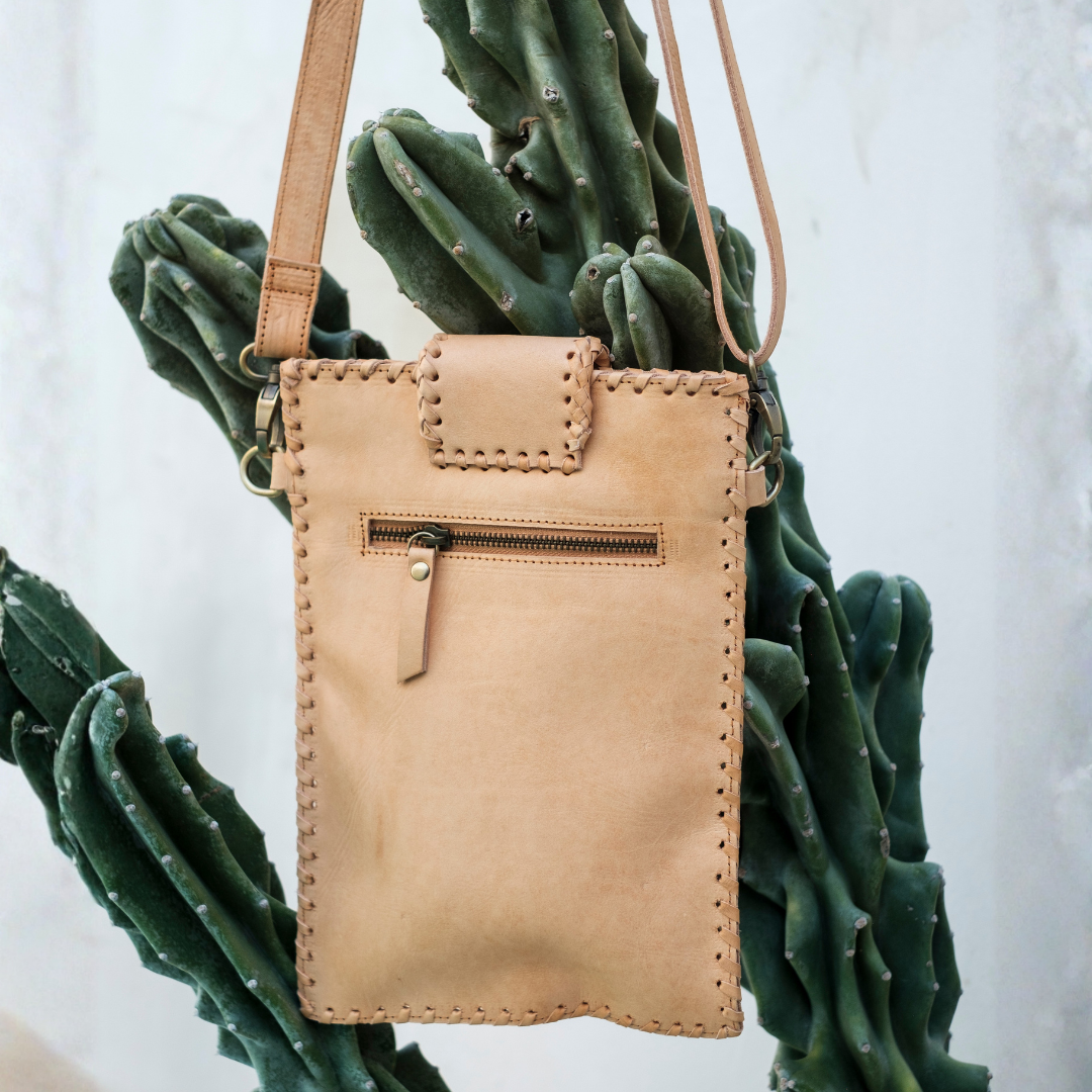 Blossom Small Crossbody Bag from House of Hide in light tan leather with front zip pocket being displayed against green cactus backdrop