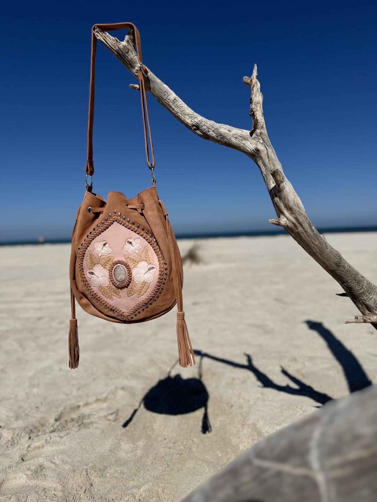 Blush Cow Suede Western Crossbody Bag – Elegant blush cow suede handbag featuring hand-painted hibiscus flowers, silver studs, and adjustable strap for western-inspired chic.