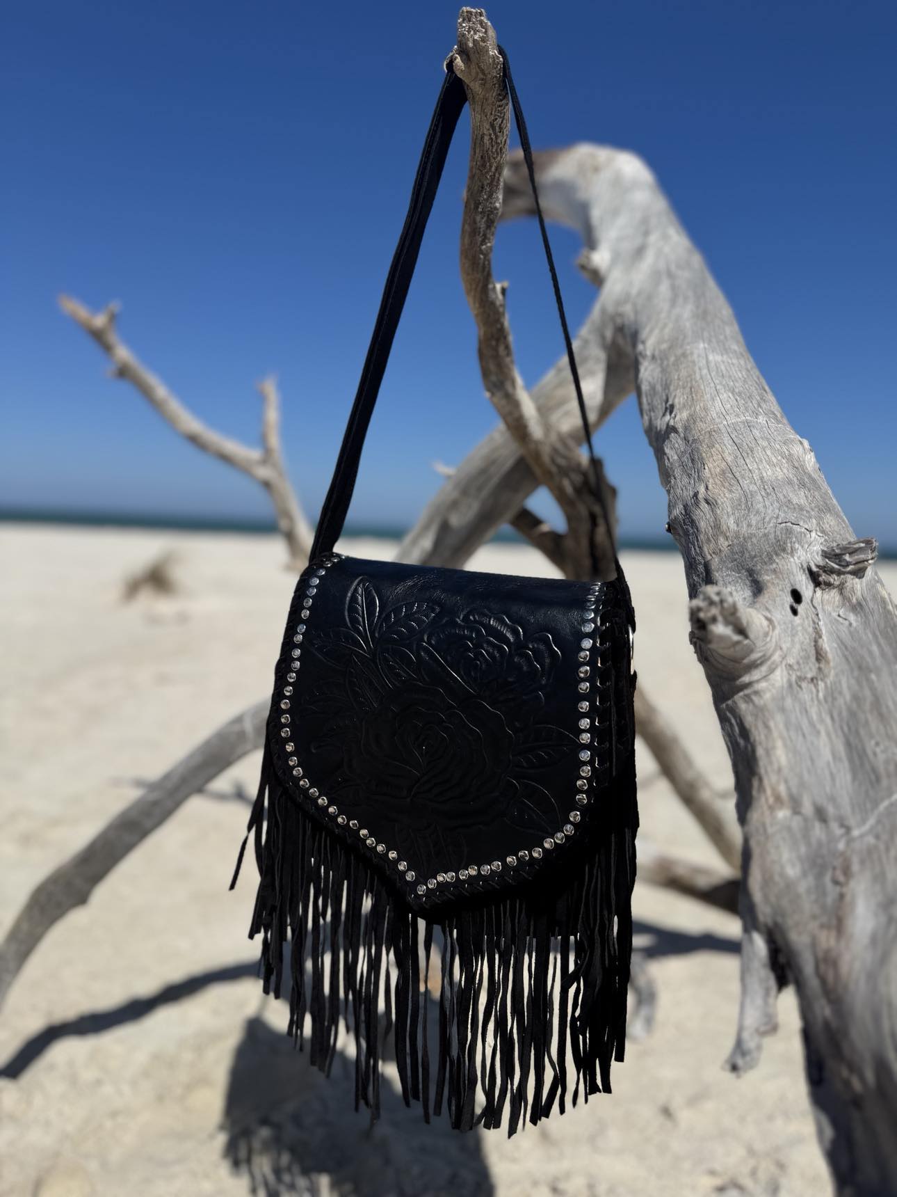 Boho-inspired black leather handbag with vintage charm, stones, and flowing tassels for a unique, western touch.