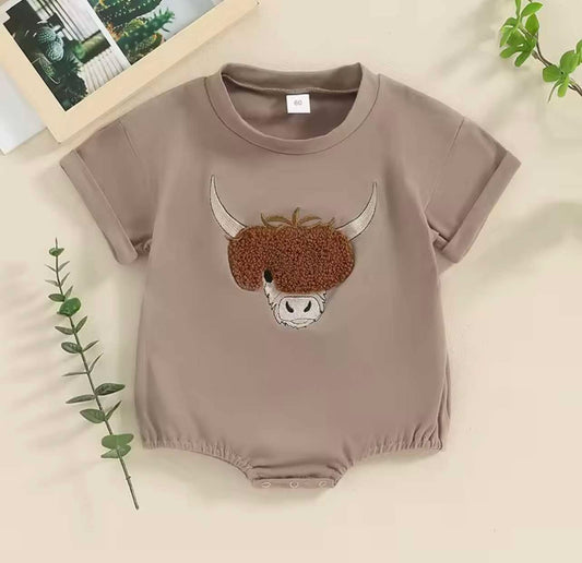 Brown cow embroidered baby onesie with short sleeves, laid flat on rustic wooden background
