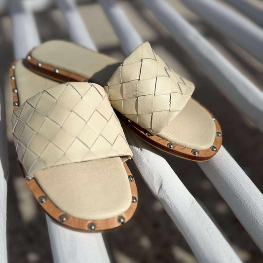 Beige woven sandals with brown accents on a white metal railing.