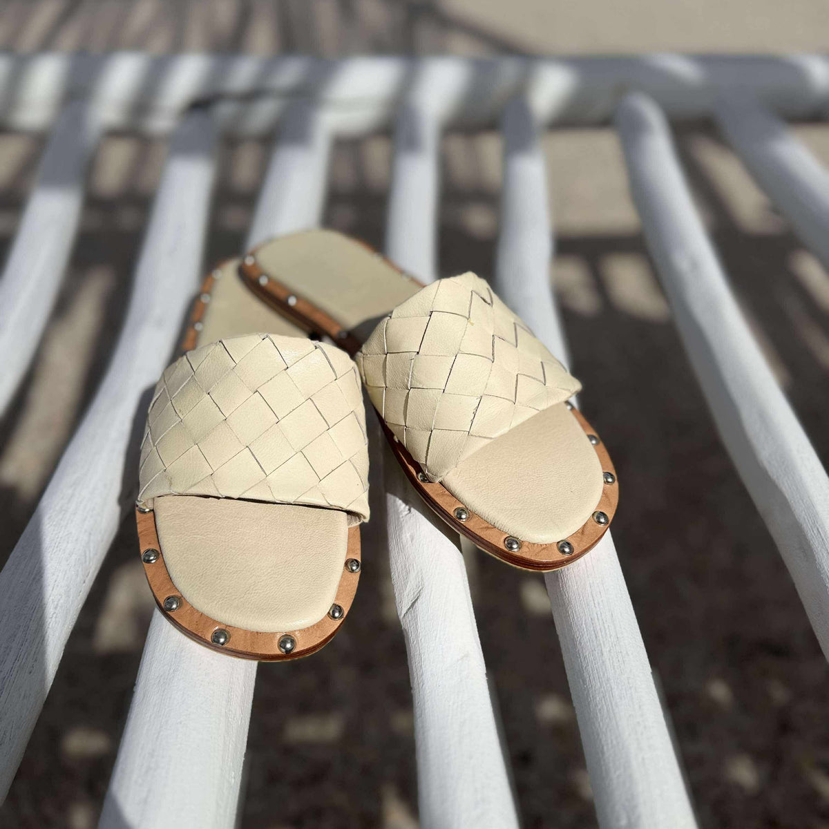 Pair of beige sandals with woven design on a white chair by a poolside.