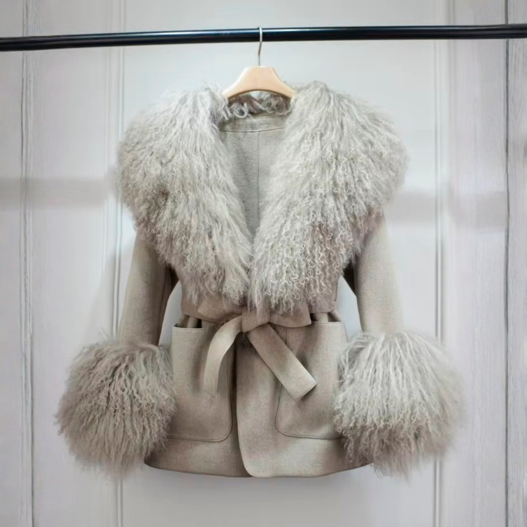Cashmere Jacket from House of Hide in soft neutral grey wool and cashmere construction, removable Mongolian sheep fur collar and cuffs for versatile styling and easy cleaning, adjustable tie belt, patch pockets, long loose trench fit on styled backdrop