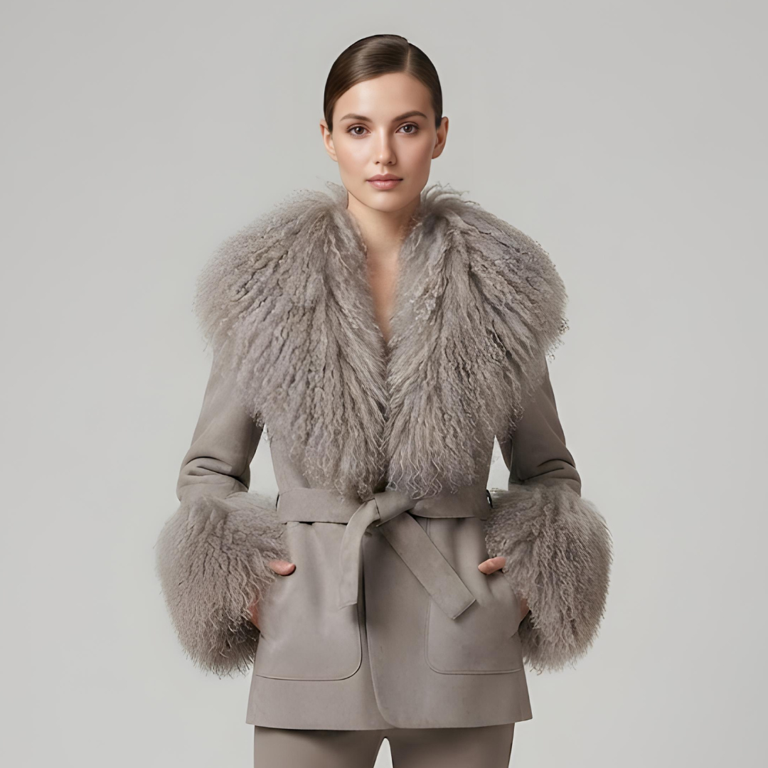 A woman wears Cashmere Jacket from House of Hide in soft grey wool and cashmere blend with detachable Mongolian sheep fur collar and cuffs, adjustable tie belt creating tailored shape, patch pockets, long loose trench silhouette being styled in editorial fashion photography as effortlessly elegant neutral layering piece