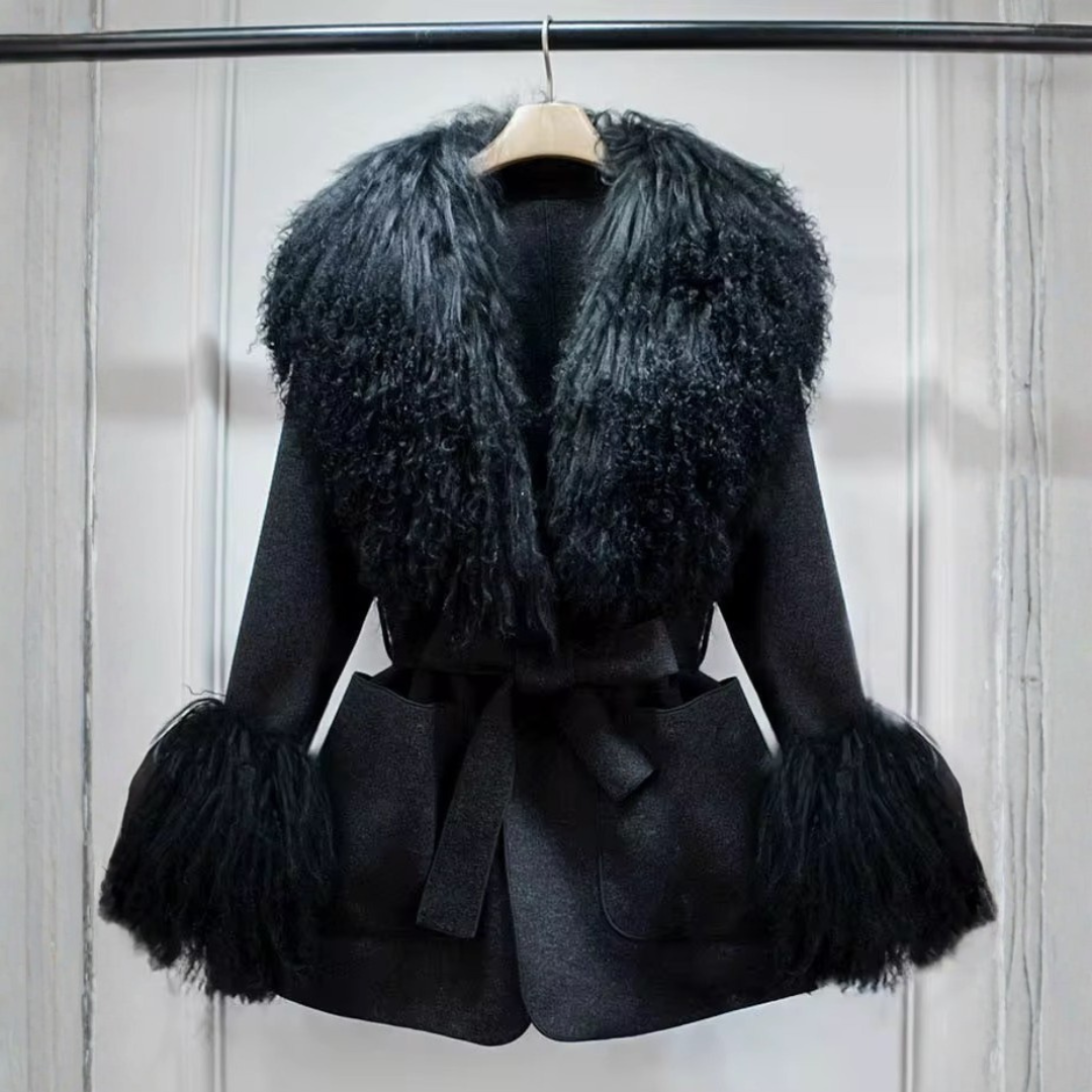 Cashmere Jacket from House of Hide in soft midnight black wool and cashmere construction, removable Mongolian sheep fur collar and cuffs for versatile styling and easy cleaning, adjustable tie belt, patch pockets, long loose trench fit on styled backdrop