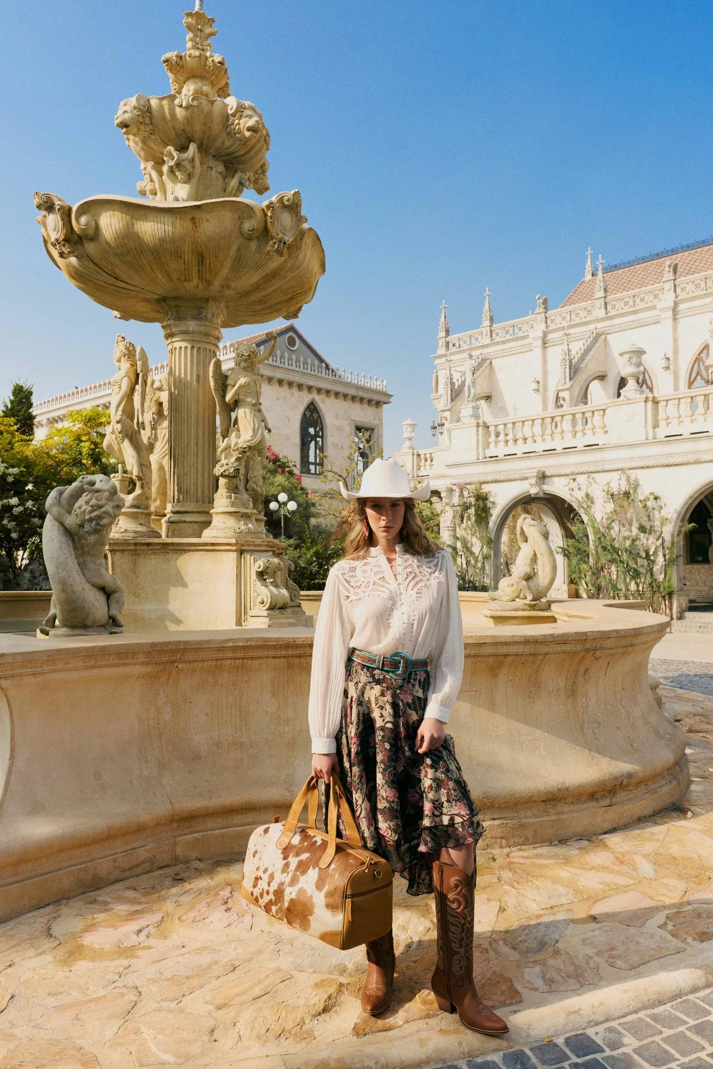Model wearing House of Hide women's western fashion in a white shirt and patterned skirt, posing in front of a fountain with elegant classical architecture