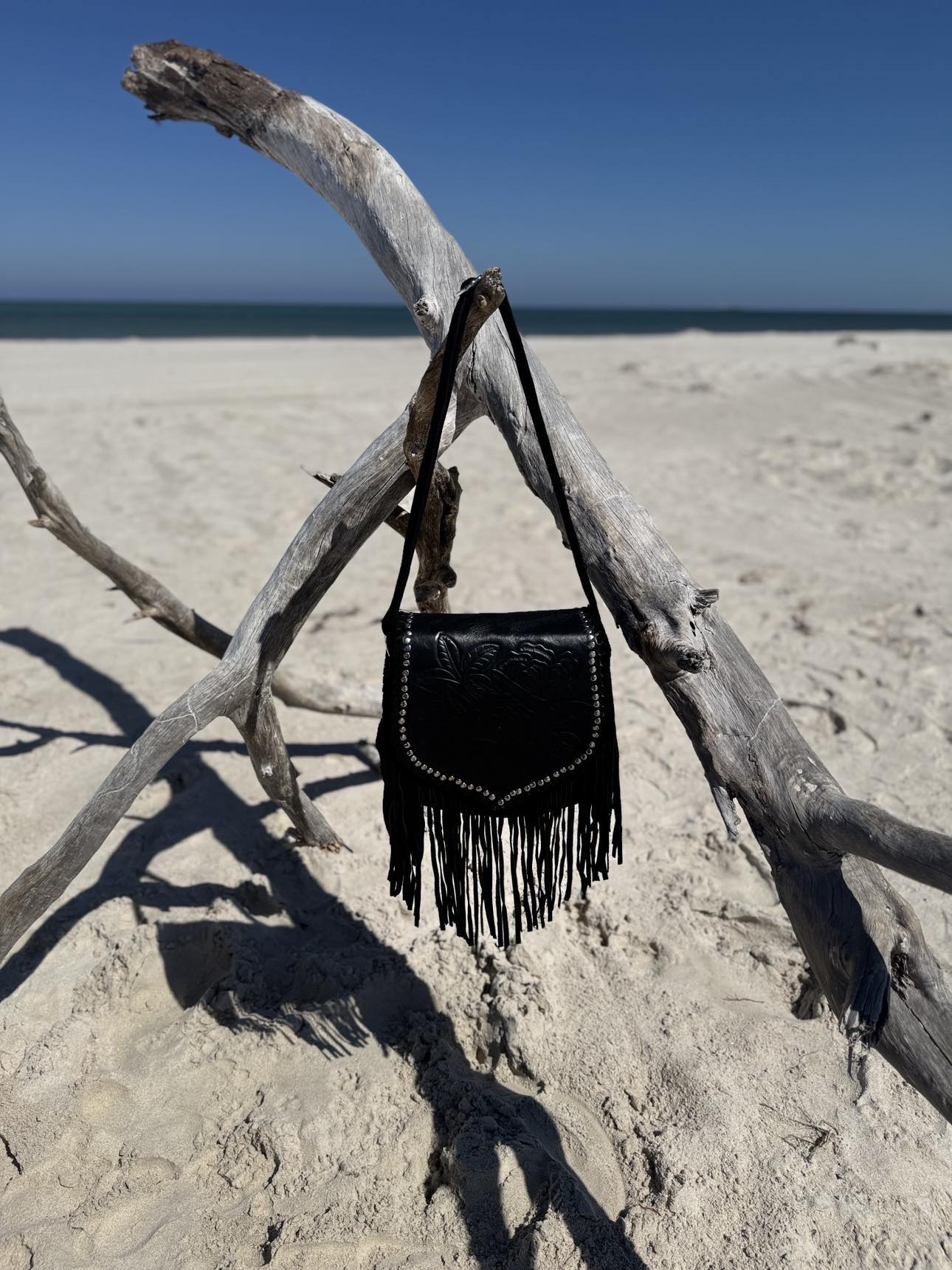 Close-up of Ebony Wild black leather handbag with detailed stone embellishments and flowing fringe tassels.