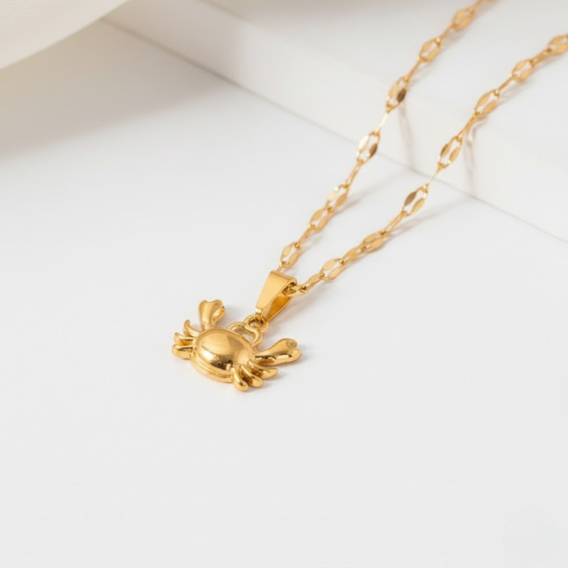 Close-up of the CrystaCrab Charm Necklace featuring a polished gold-plated crab pendant on a reflective chain.
