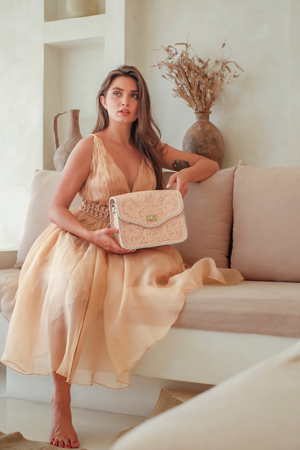 Model opening hand-tooled tan leather clutch with floral design. Bridesmaid or bridal clutch in cream woven edge leather