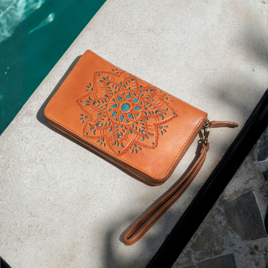 House of Hide Desert Mandala Wallet in tan leather with cutout mandala design and wrist strap being displayed on light stone surface next to teal pool
