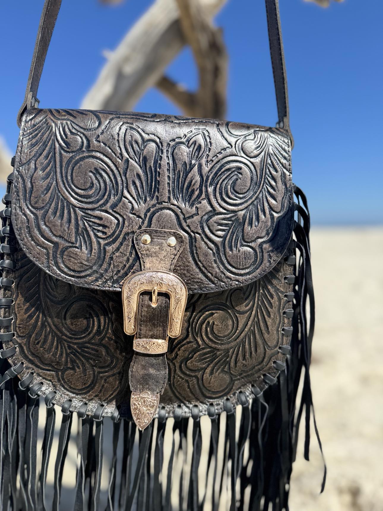 Detailed shot of the hand-tooled leather work on the Blackstone Crossbody, accentuated by the sleek black design and tassels.