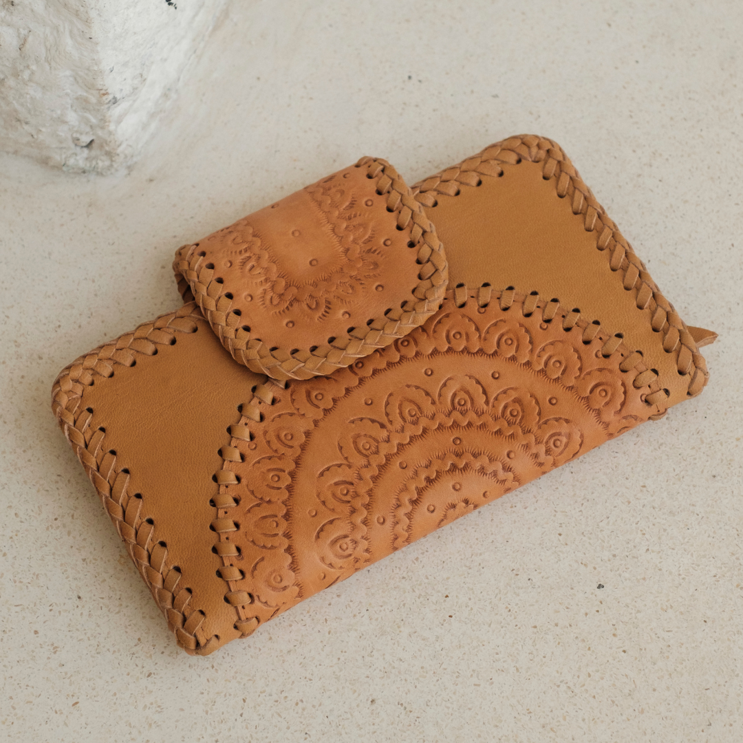 Dustwood Carved Wallet from House of Hide in tan leather with hand-tooled floral patterns and braided stitching being displayed on light beige textured surface