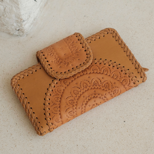 Dustwood Carved Wallet from House of Hide in tan leather with hand-tooled floral patterns and braided stitching being displayed on light beige textured surface