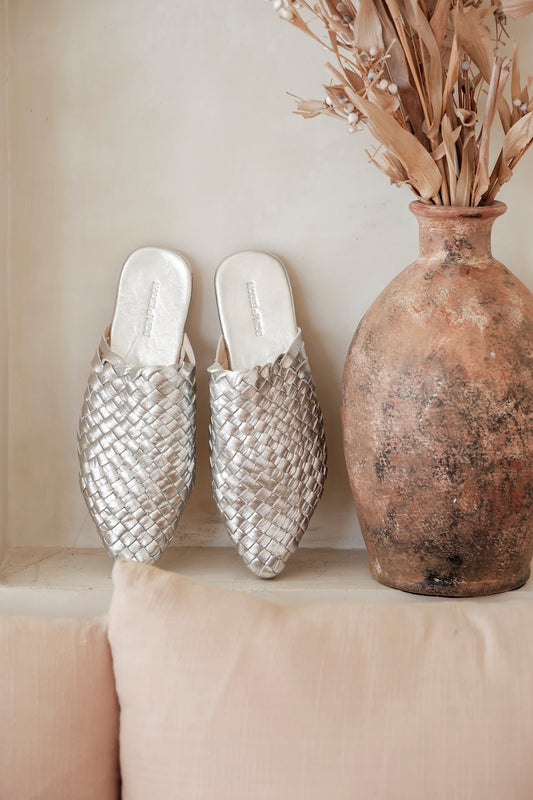 Flat lay of ethically handmade women’s leather slip-on slides in silver, featuring closed toe design and woven craftsmanship for boho-chic style