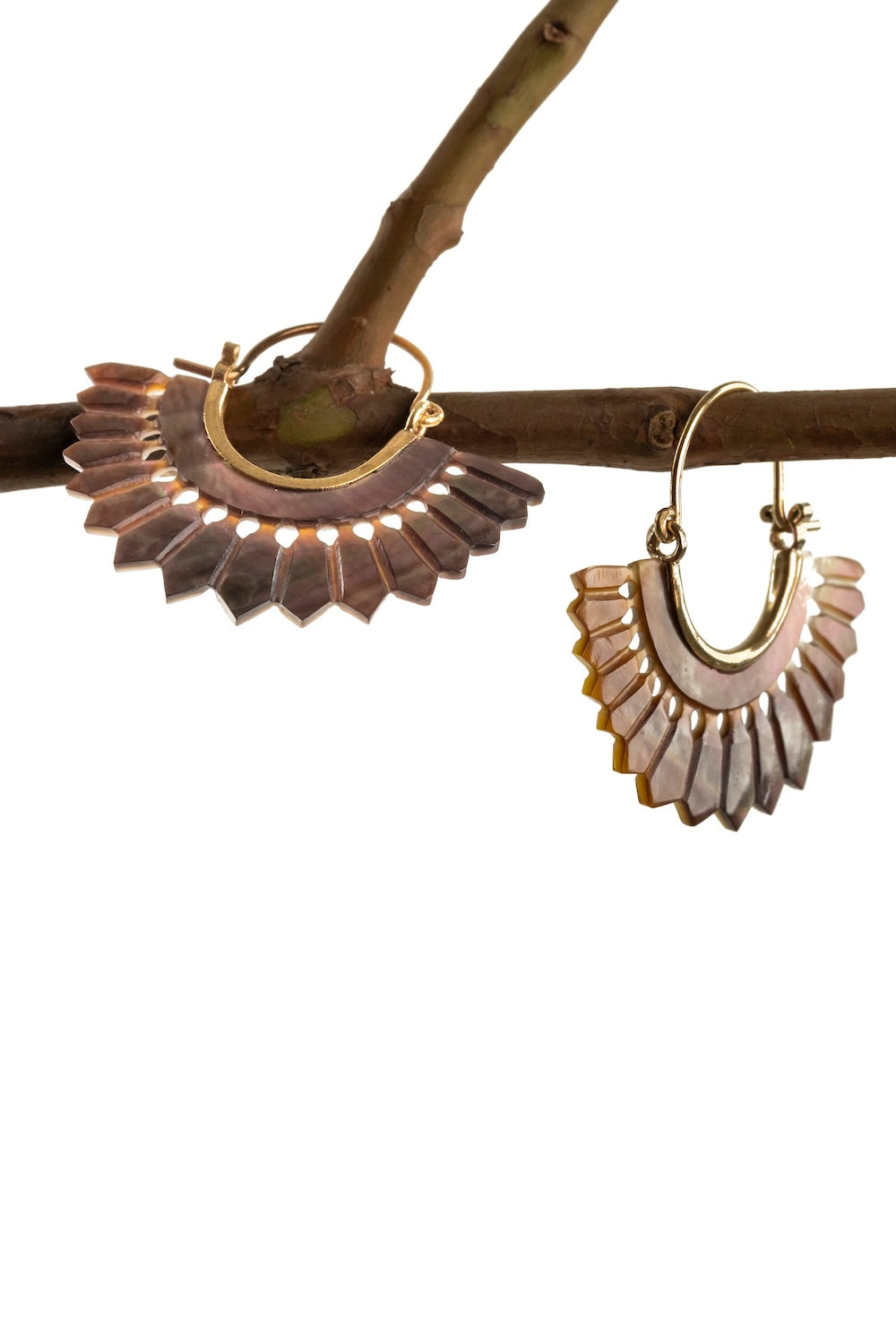 Fan-shaped brass and shell earrings styled on a natural timber twig, highlighting their earthy tones and handcrafted detail.