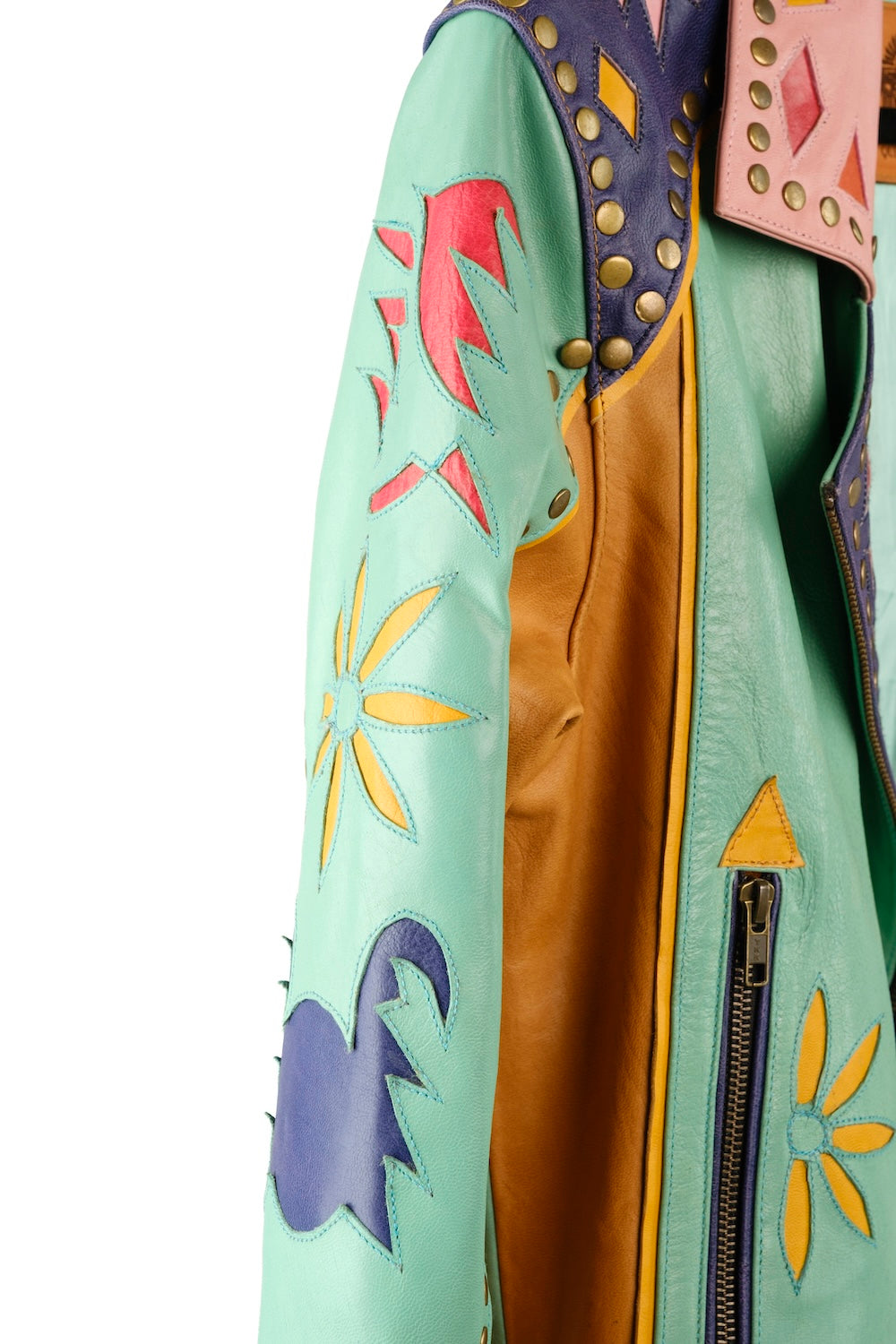 Festival leather jacket for women – bright patchwork, Western studs, and a desert sunrise stitched on the back. Ethically made.