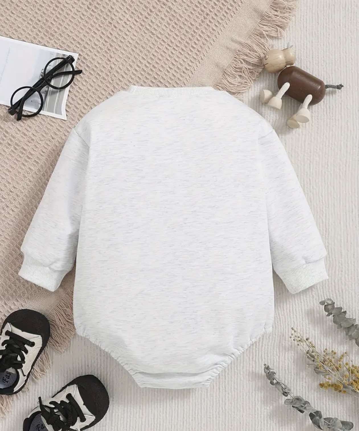 Flat lay of a grey Fresh Out of the Chute baby romper featuring cattle and letter print design on a neutral background.
