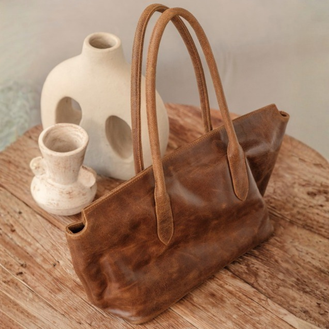 Frontier Tote Bag from House of Hide in brown leather with dual top handles being displayed on rustic wooden table with cream ceramic vases