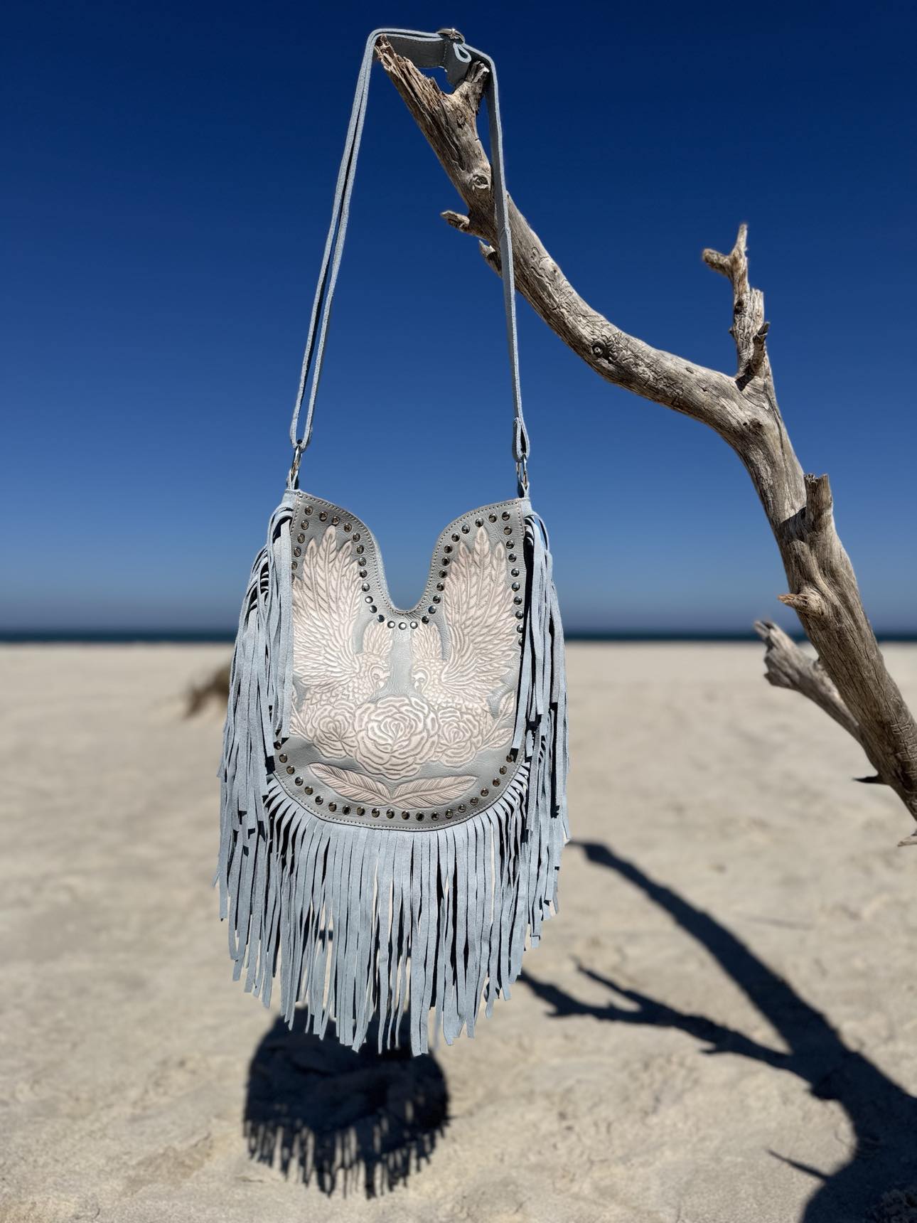 Handcrafted light blue fringe handbag, boho chic with western saddle accents for cool summer tones.