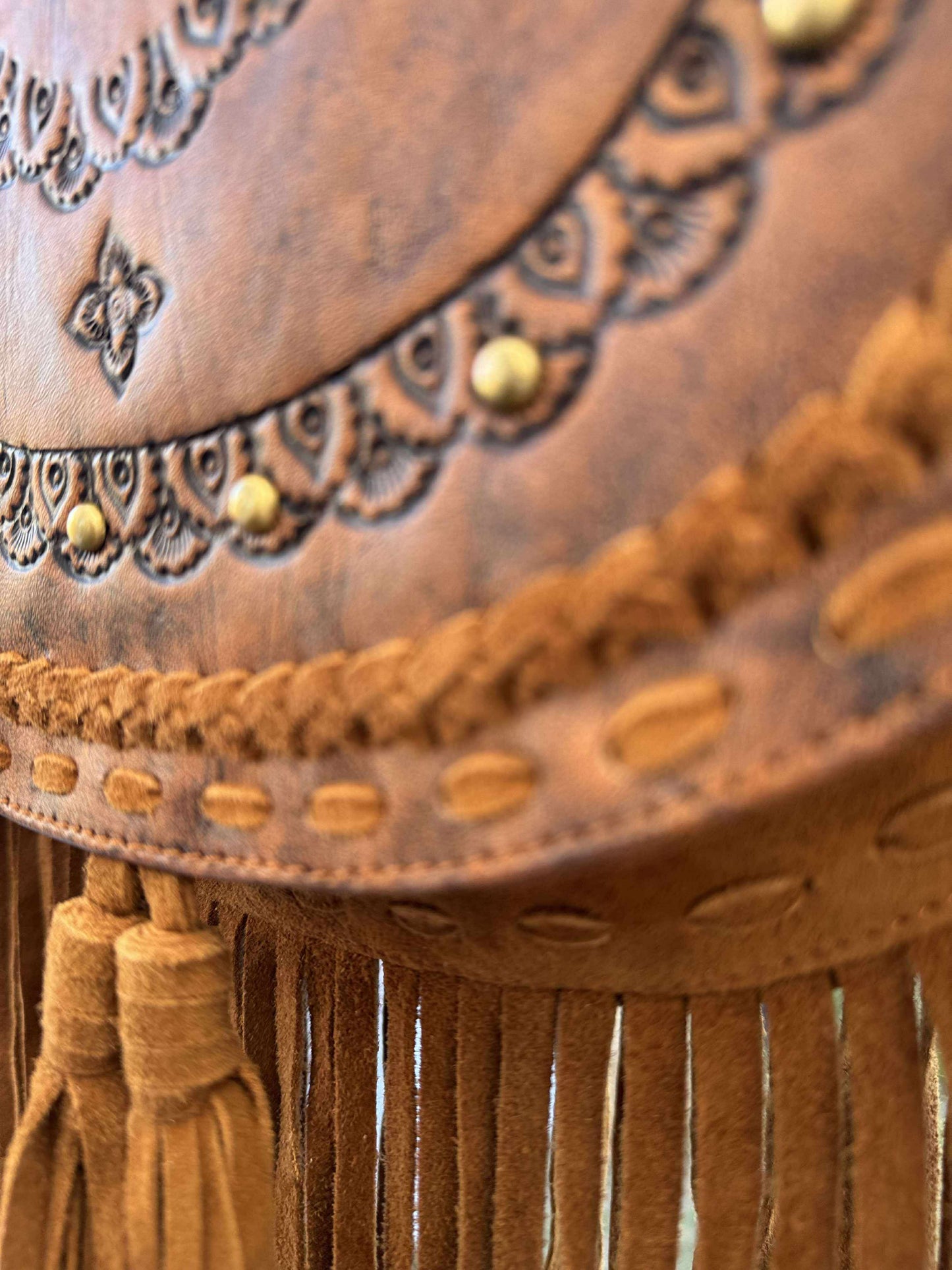 Close-up of the SadieFringe Bag, showing hand-tooled cowhide flap, earthy leather tones, and one-of-a-kind turquoise stone centerpiece.