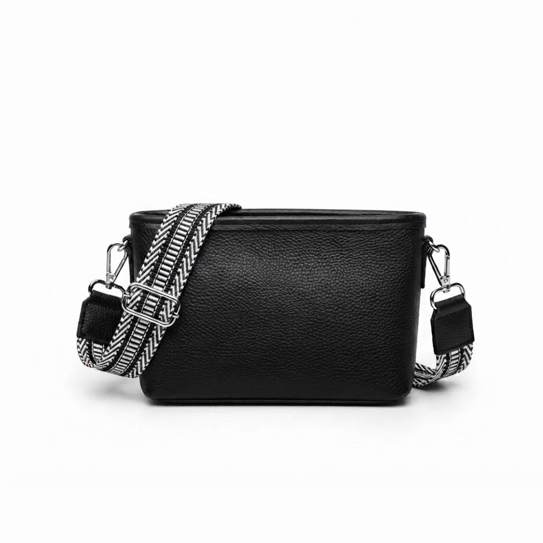 A black pebbled leather crossbody bag with a wide, woven black-and-white patterned shoulder strap and silver-tone hardware, shown against a plain white background.