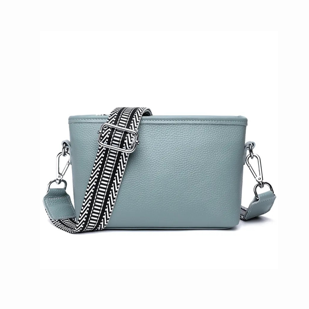 A light blue pebbled leather crossbody bag with a wide, adjustable black and white patterned woven strap and silver-tone hardware, shown on a plain white background.